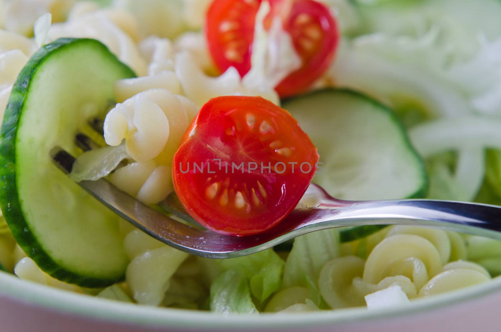 Close up (macro) of a fork, lifting pasta and salad from a bowl.  Landscape (horizontal) orientation.