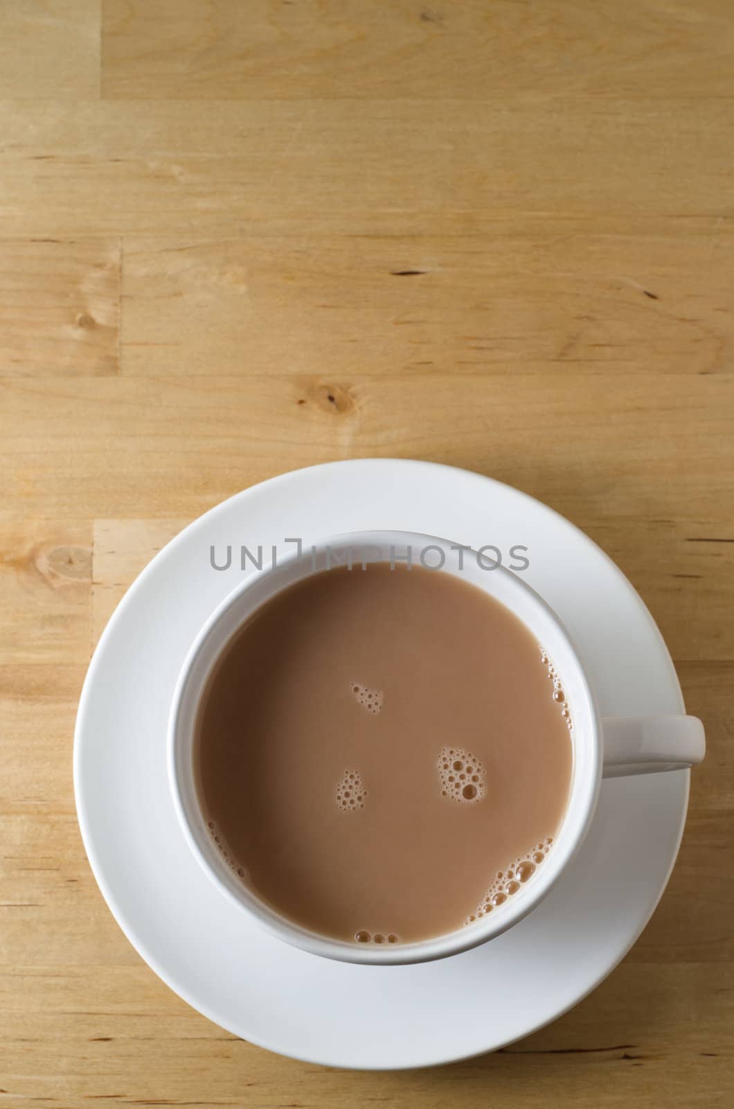 Overhead shot of a cup of tea, with saucer on old, scratched light wooden table with copy space in top frame.  Vertical (portrait) orientation.