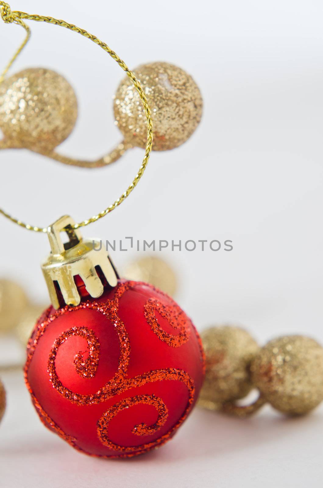 A patterned red bauble, with gold glittery balls in soft focus off-white background.  