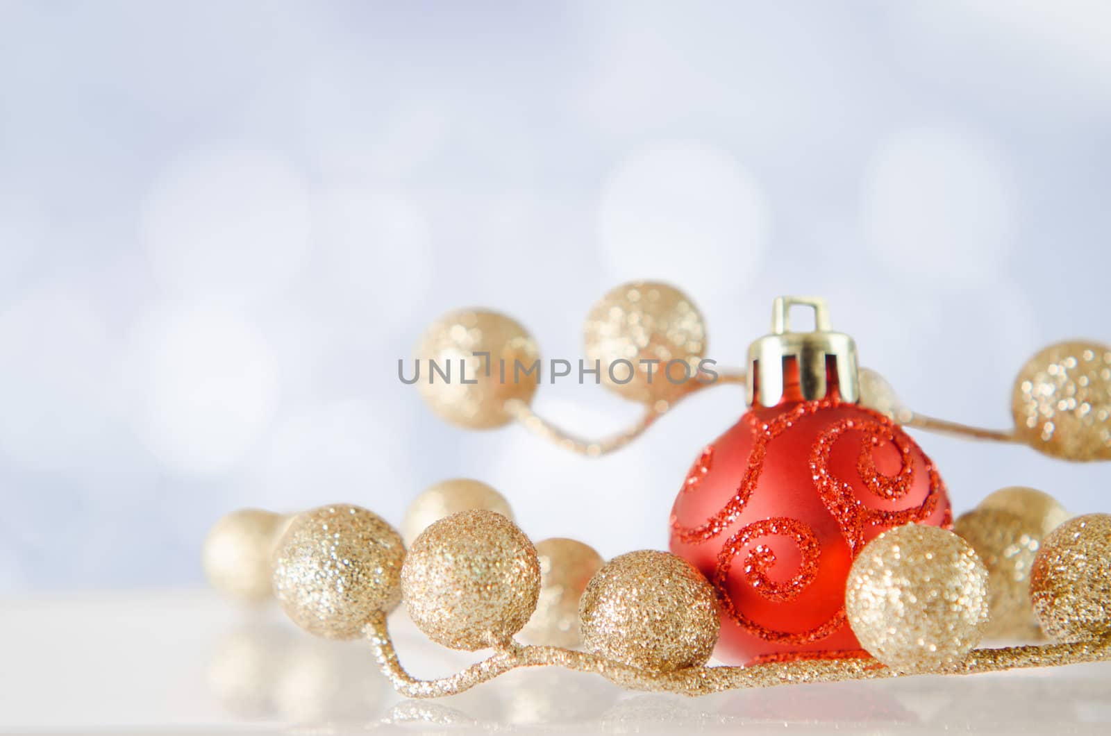 A red bauble with gold glitter balls on an 'icy' reflective surface, with blue and white snow-effect bokeh background.
