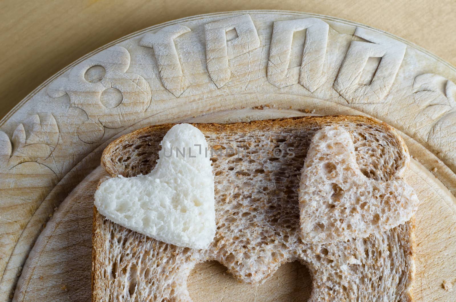 Close up of white and brown wholemeal bread hearts and slice on an old vintage bread board with the word 'bread' embossed in the wood.  