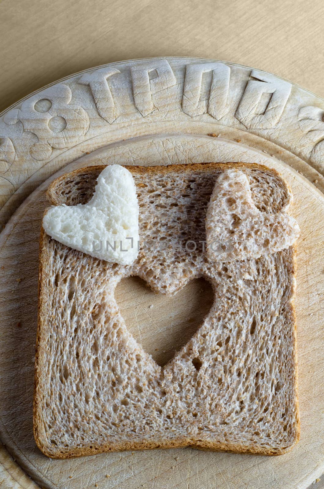 Overhead shot of white and brown wholemeal bread hearts and slice on an old, scratched vintage bread board with the word 'bread' embossed in the wood.  