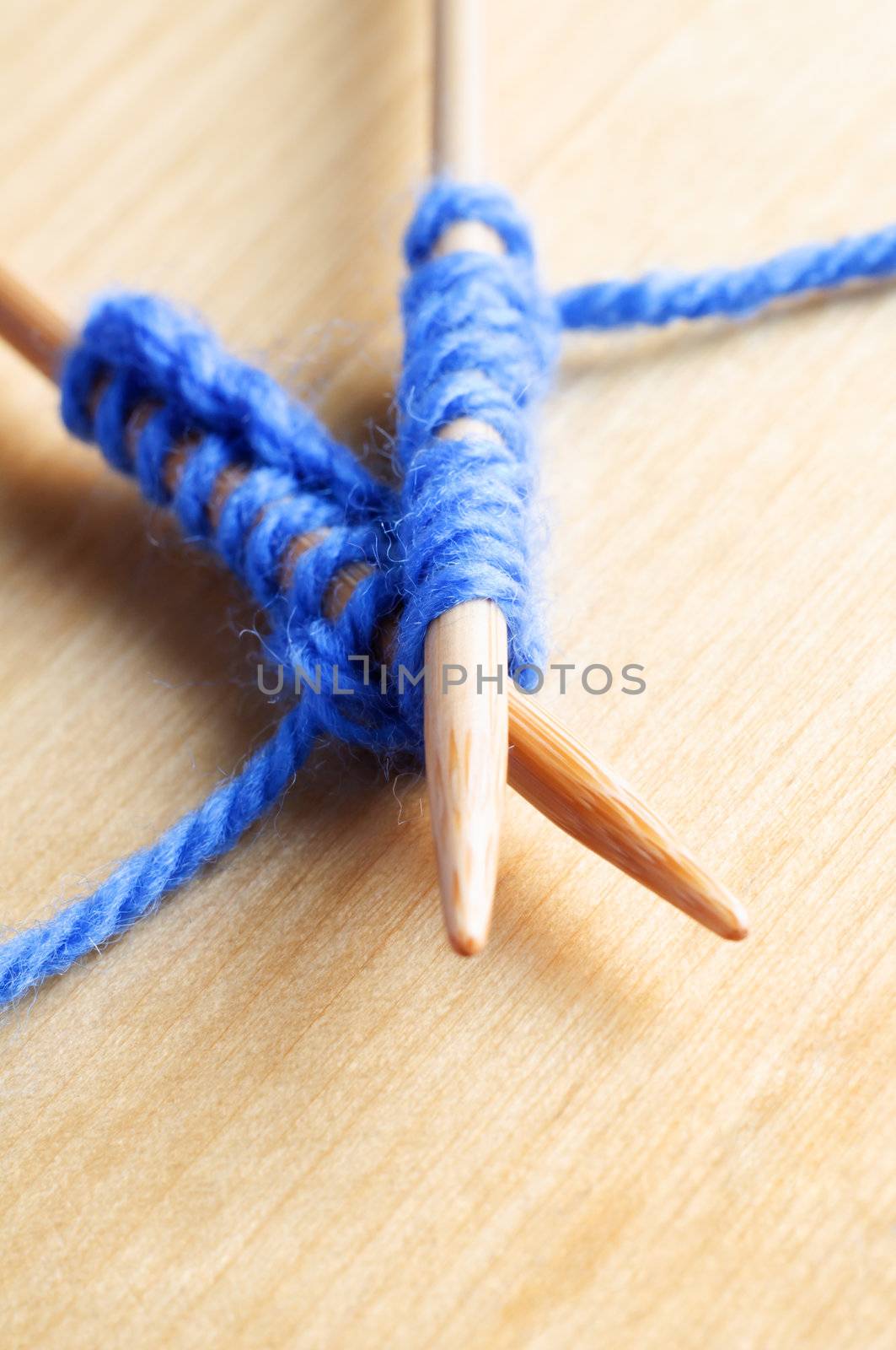 Close up (macro) of a pair of crossed  knitting needles laid on a wooden table holding stitches in pale blue wool.