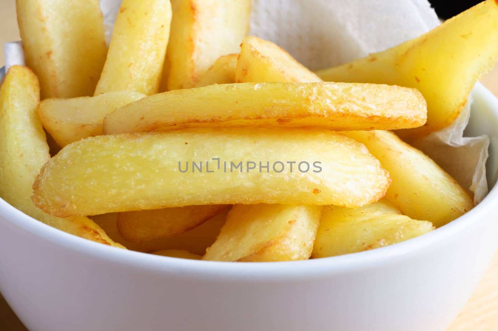 Close up (macro) of a bowl filled with chips (french fries) with absorbent paper.