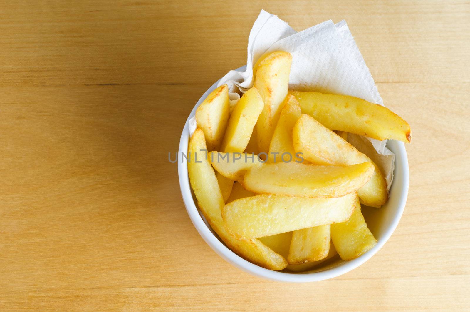 Overhead shot of a bowl of chips (french fries) on a wooden table.  Copy space to left.