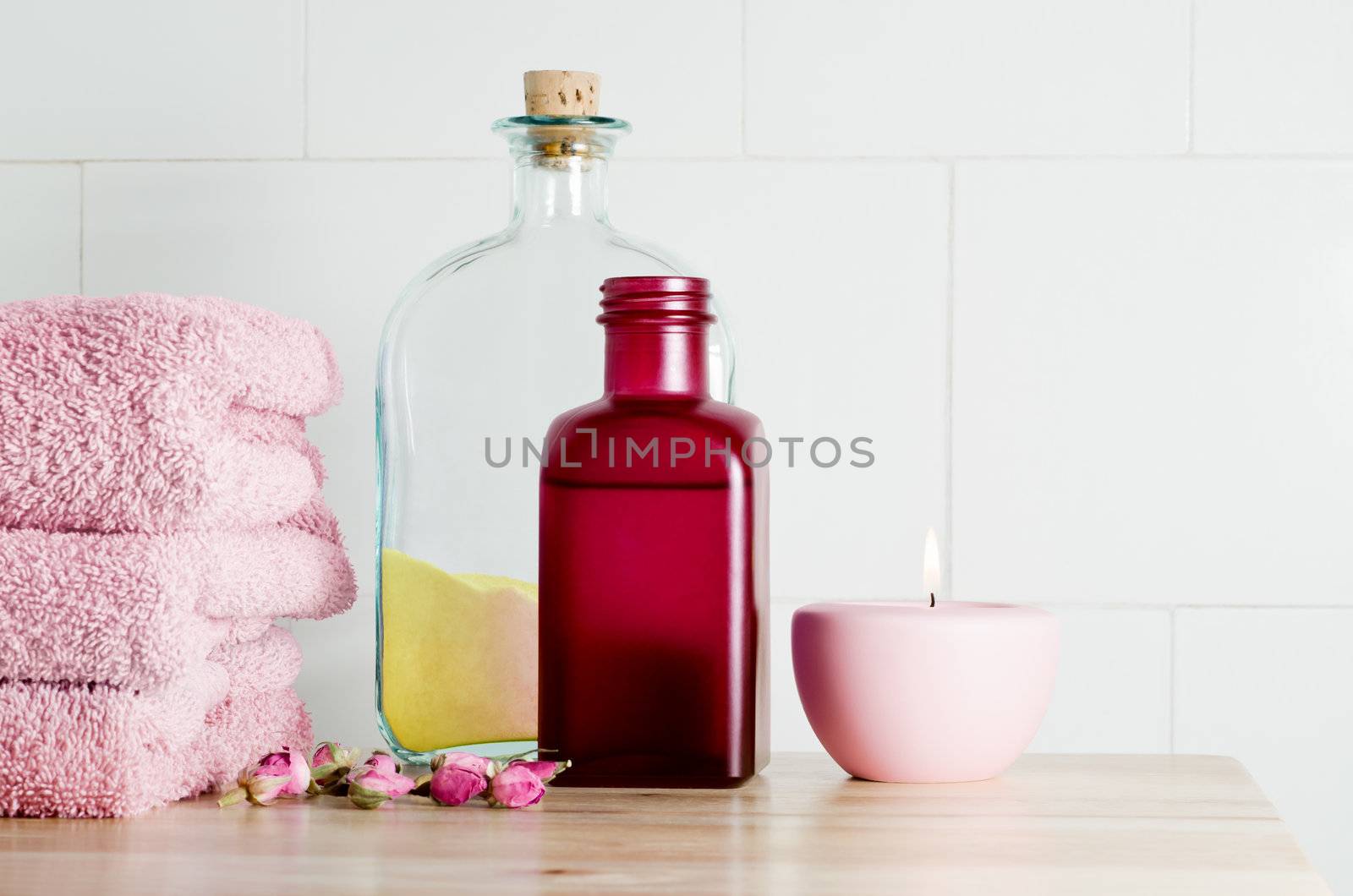 Spa bath items in pink and yellow theme on a light wooden surface against a white tiled wall which provides copy space to the upper right