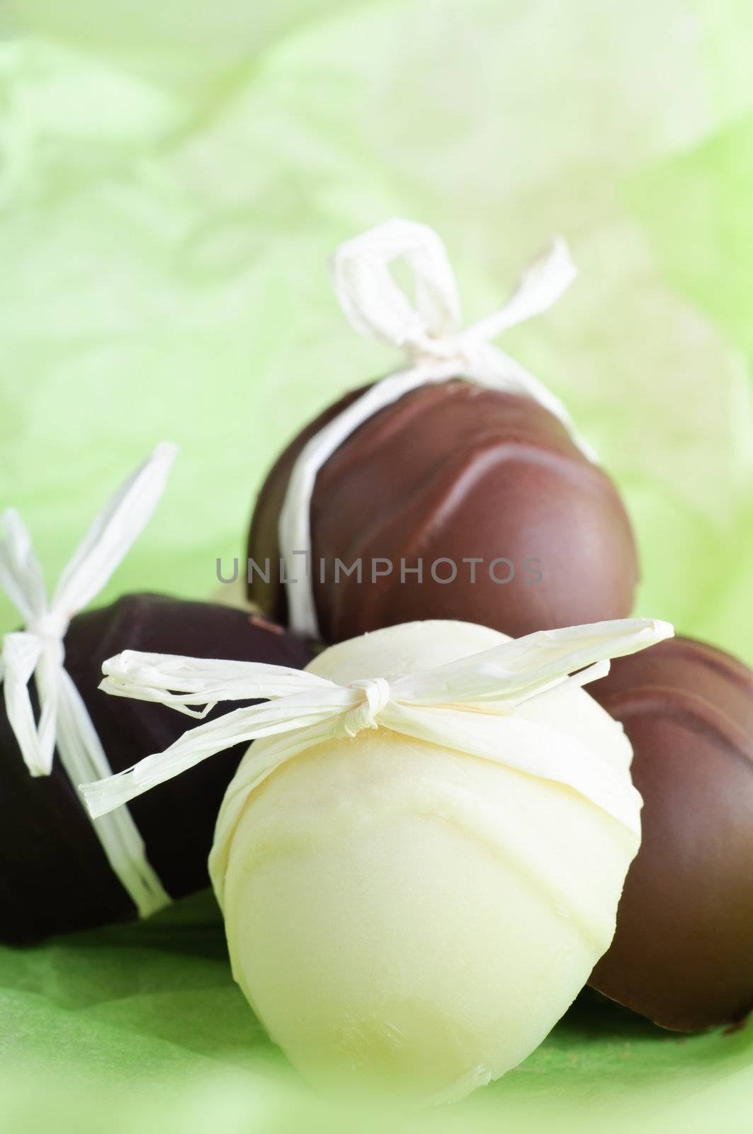 A group of home made egg shaped Easter chocolates, bow tied with raffia ribbon on a fresh, light Spring green background.