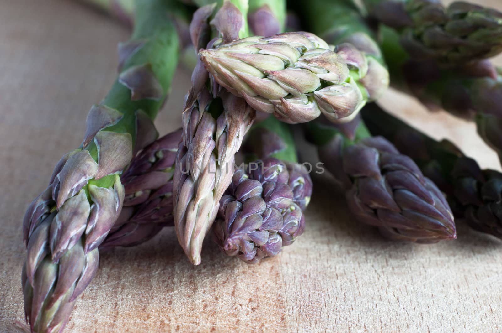 Close up (macro) of an arrangement of asparagus spears (stems) on an old, scratched, wooden chopping board.