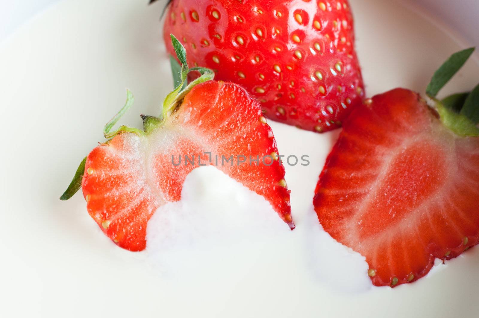 Close up (macro) of whole and halved fresh strawberries with leaves, partly immersed in double cream.  