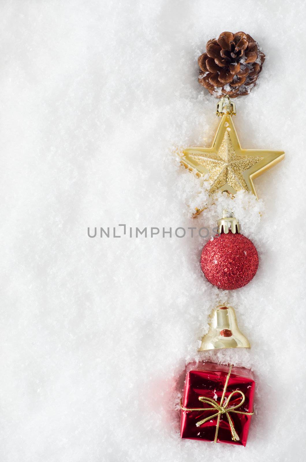 An uneven vertical line of Christmas ornaments running from top to bottom of frame, half buried in snow, on right hand side.  Copy space to left.