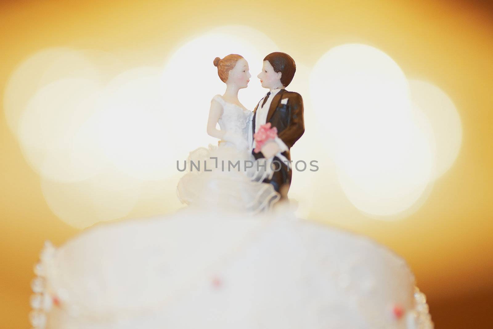 Figurines of bride and groom on a wedding cake by the bright light