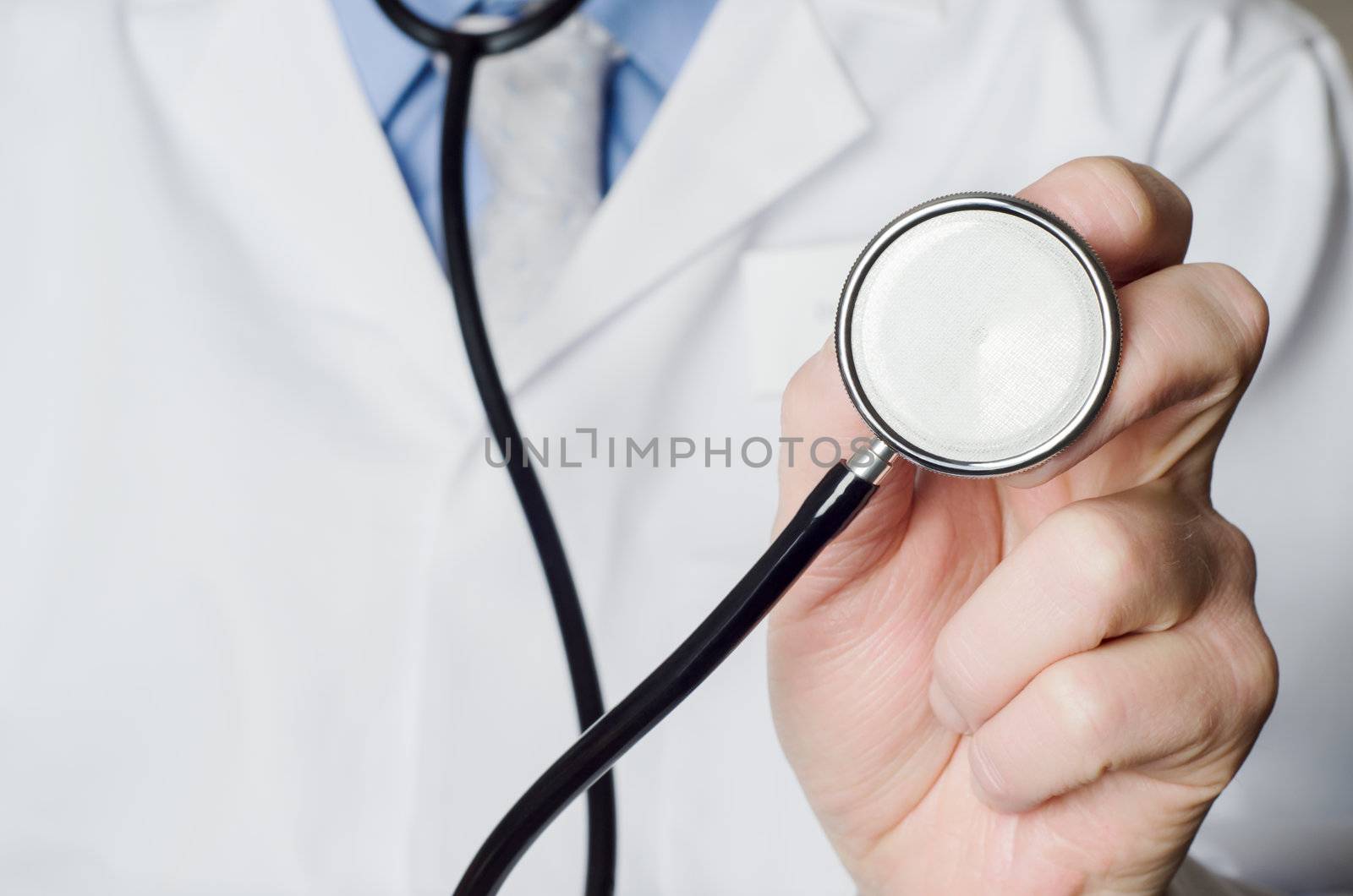 Close up of a Doctor's hand, holding a stethoscope outstretched towards the viewer.  Doctor's white coat provides space to the left side of frame.