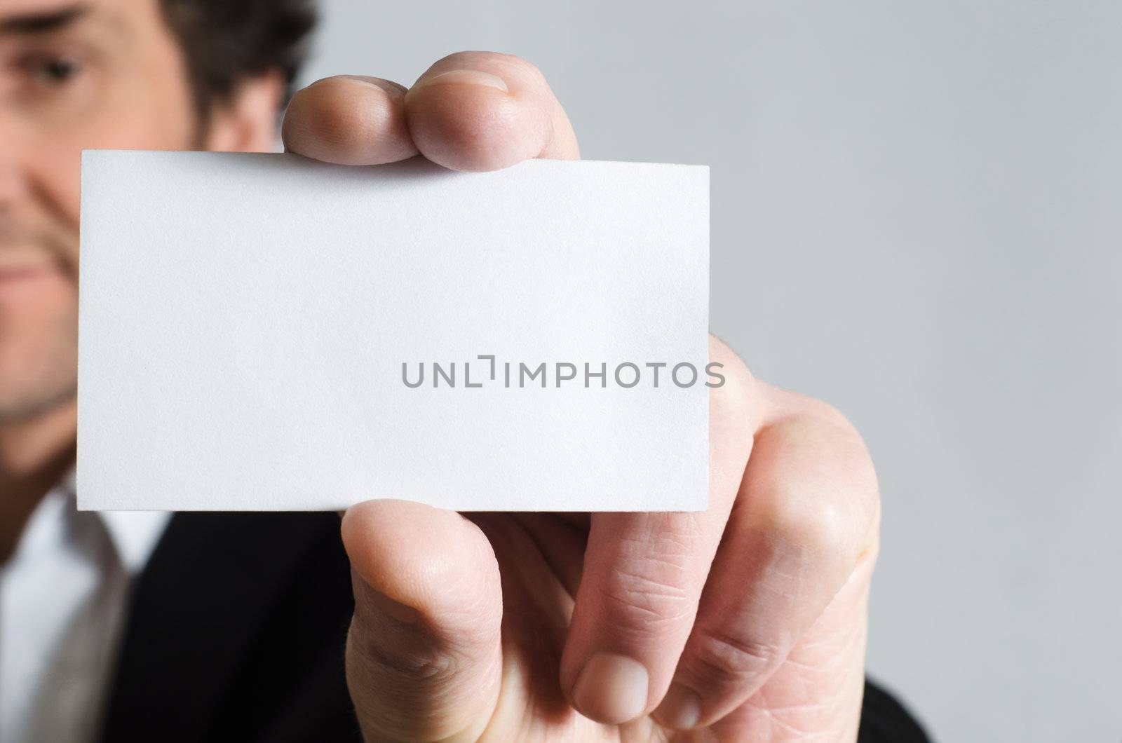 A man in a black suit with white shirt holding up a blank business card to display to viewer.