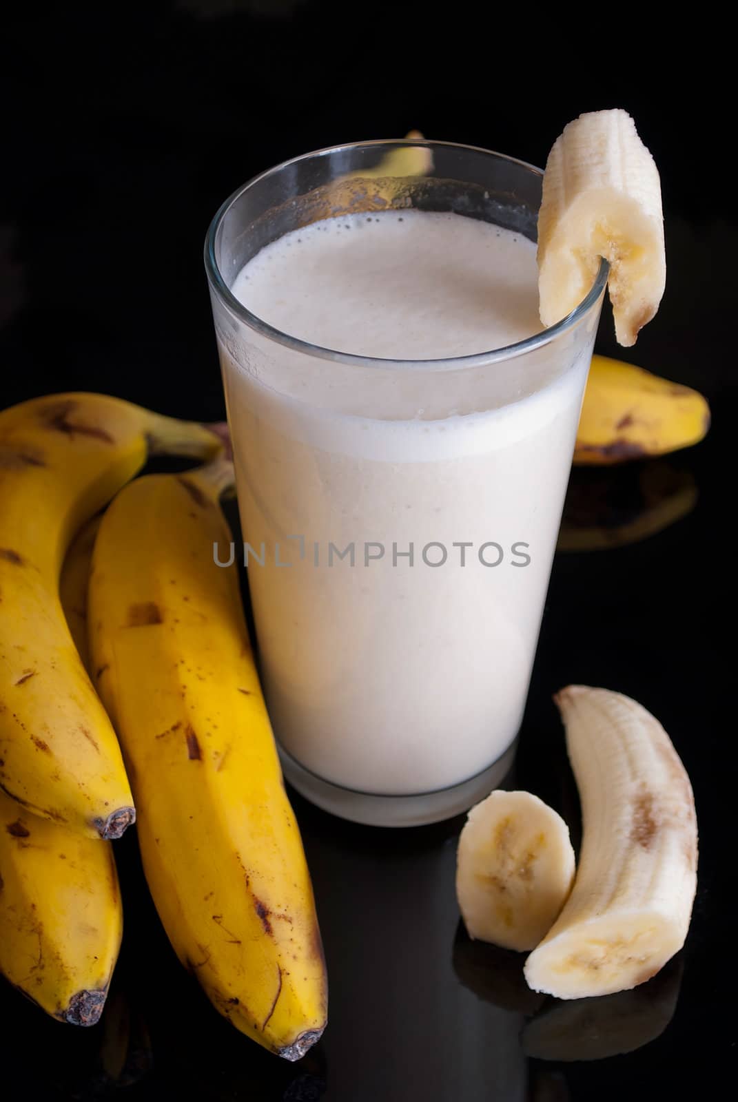 fresh banana smoothie and fruits on black background