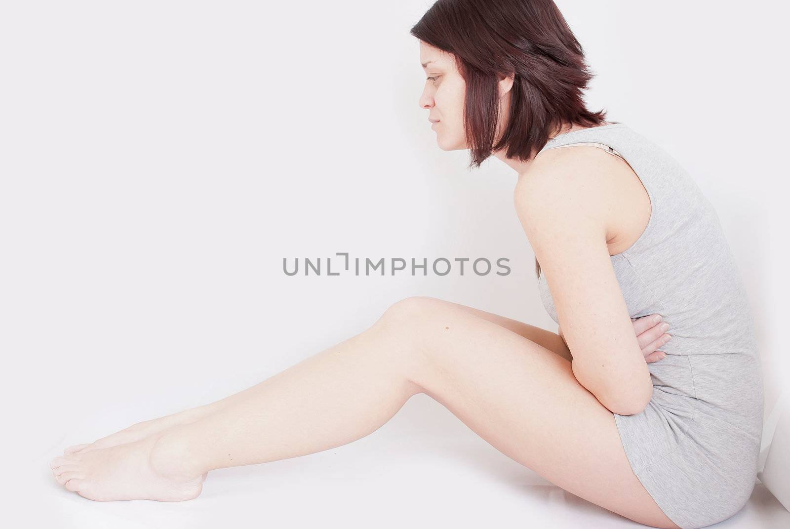 young woman with stomach pain sitting on floor holding holding her tummy