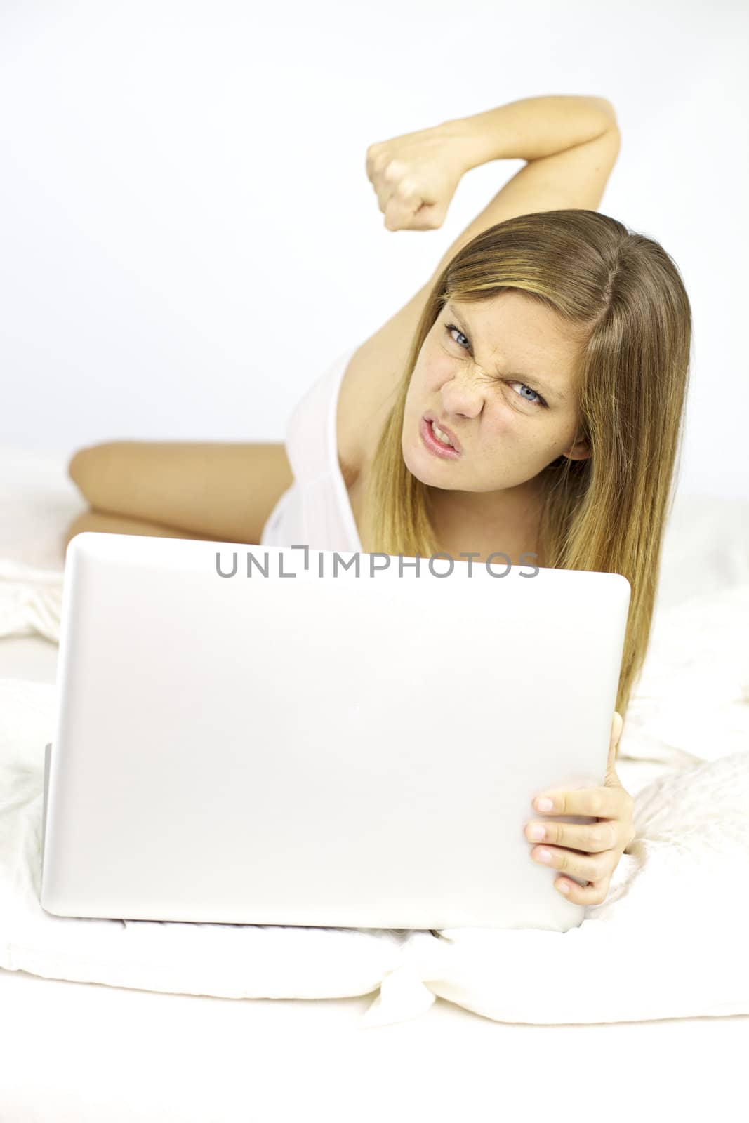 Woman in bed fighting with computer angry about technology