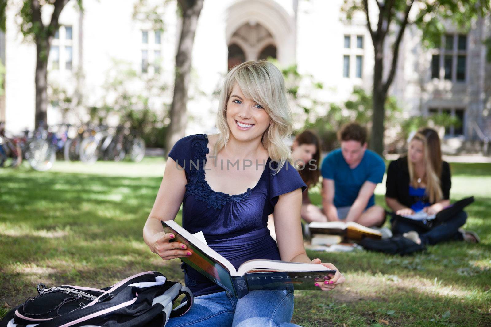 Portrait of smiling young girl with book with her classmates studying in background