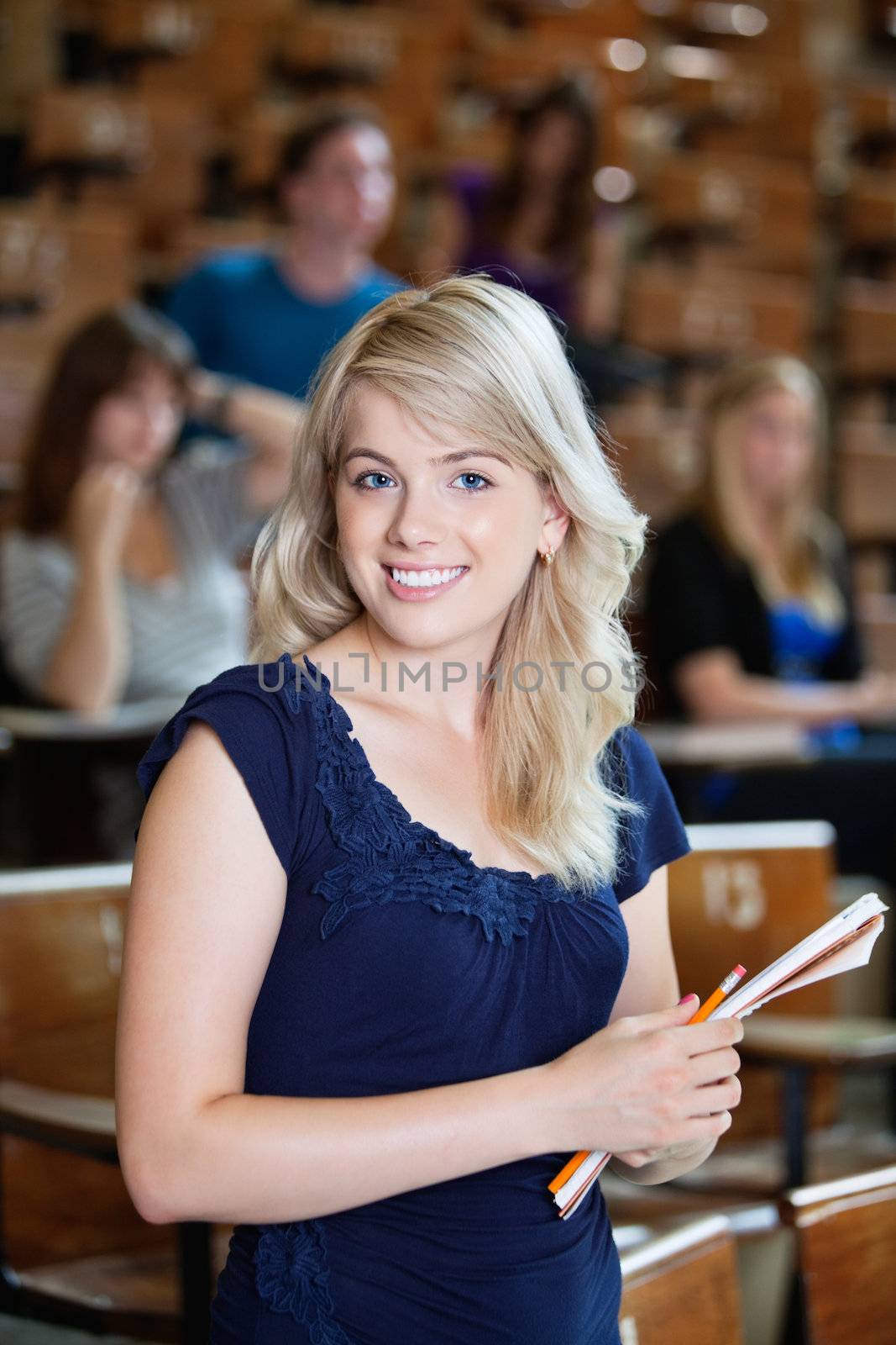Portrait of young girl standing in auditorium with classmates in background