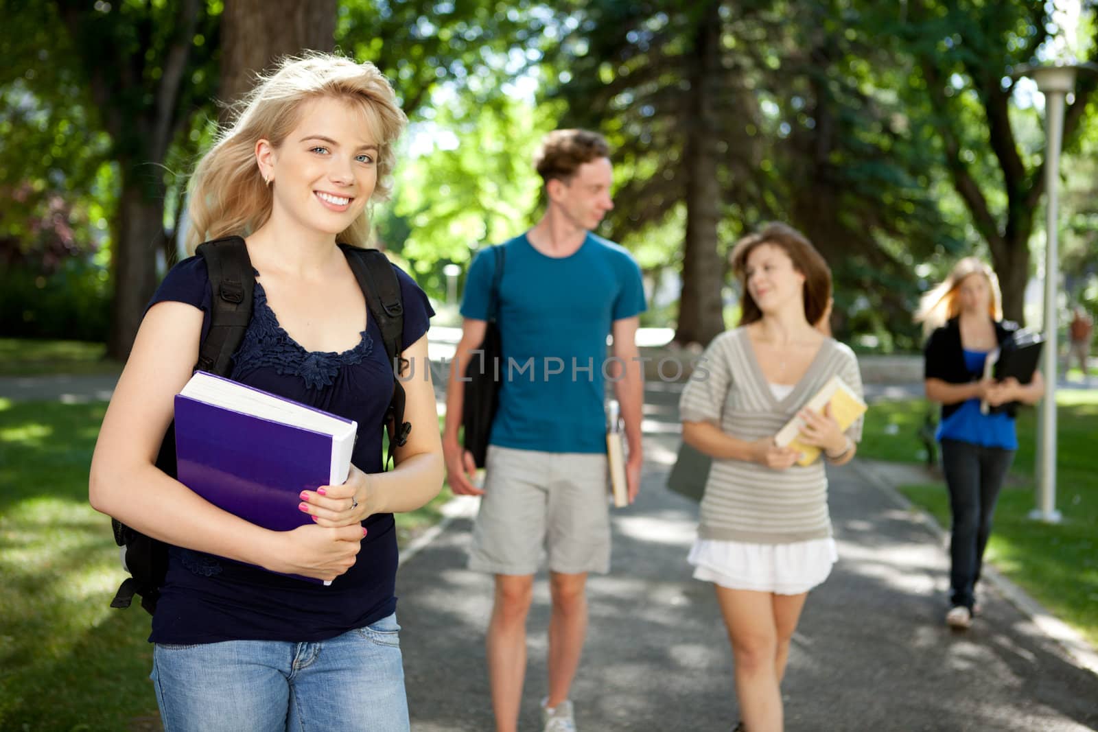 Pretty blond college girl looking at camera with friends in background