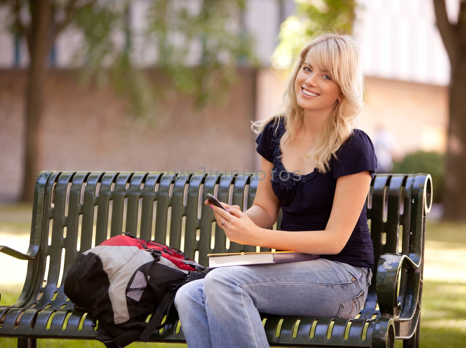 Friendly young female student sitting on a bench sending a text message