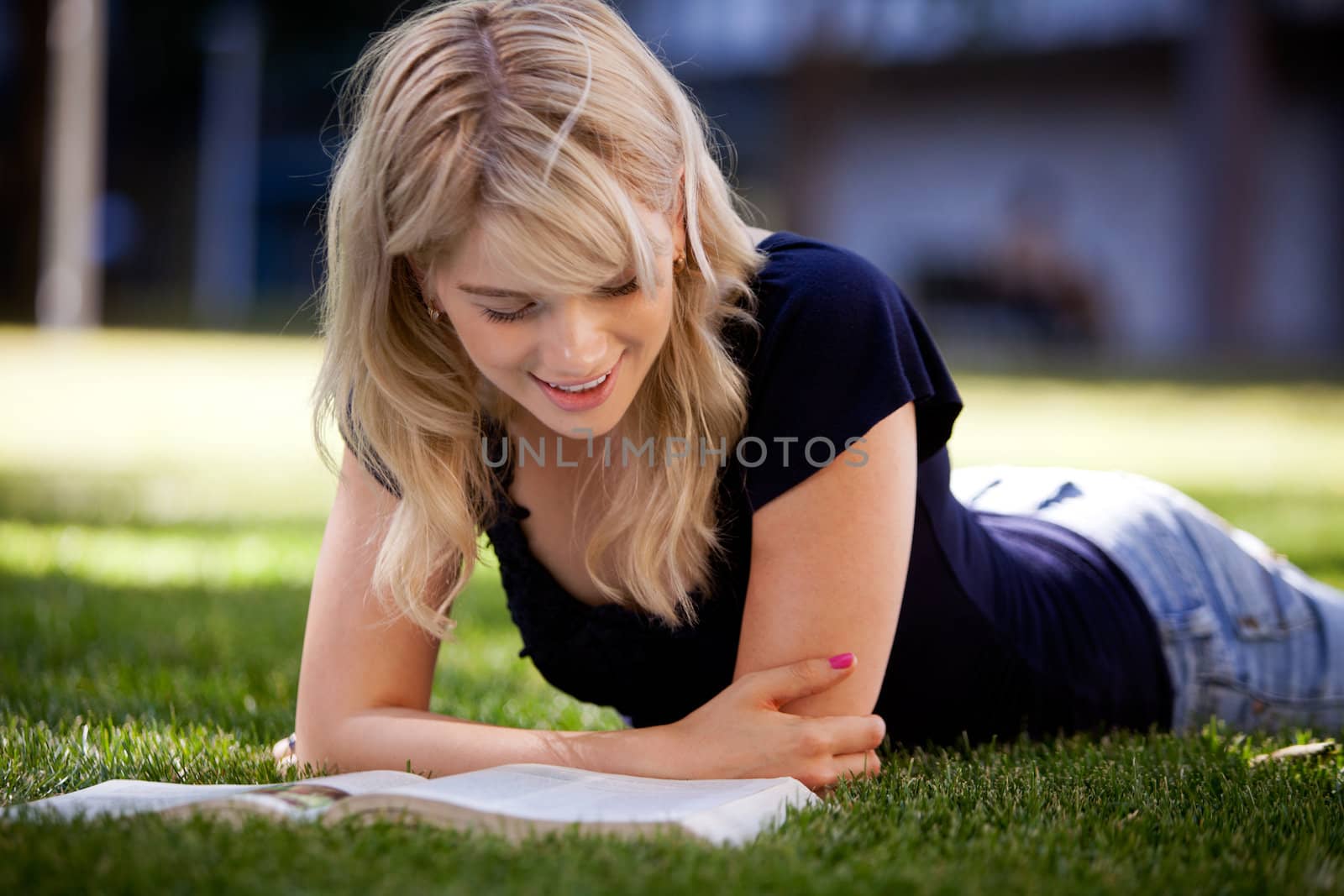 Smiling university student reading a text book outdoors