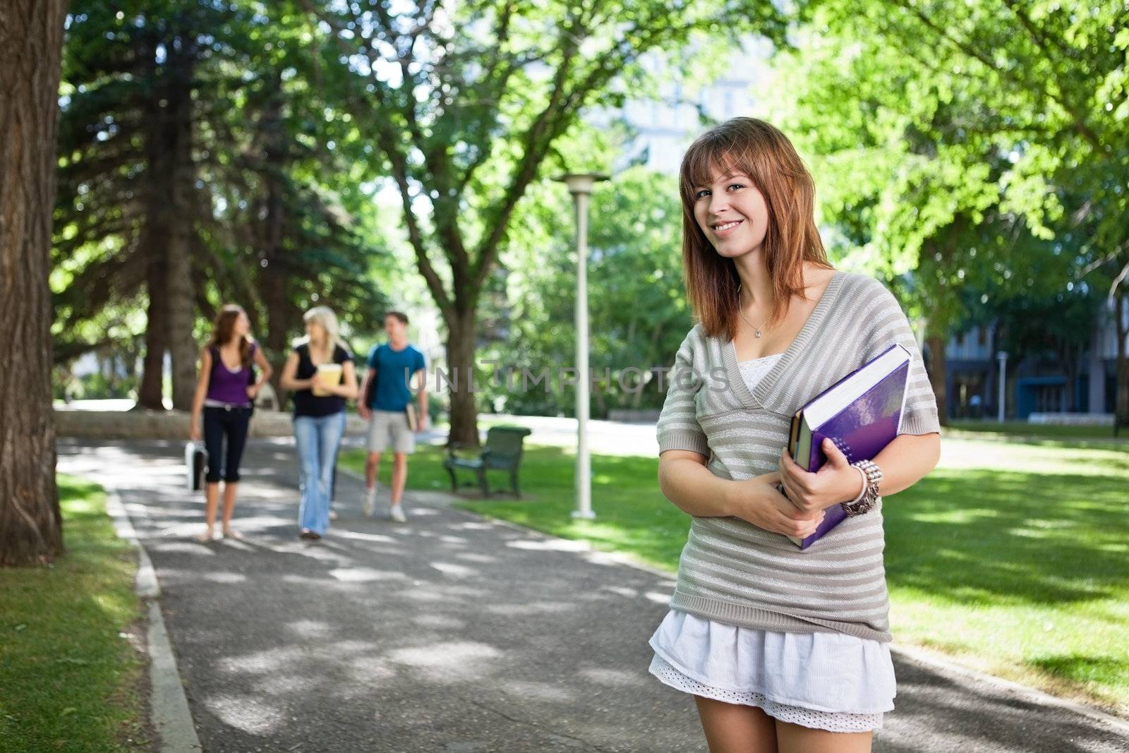 Portrait of girl standing with a book while her friends walking in background