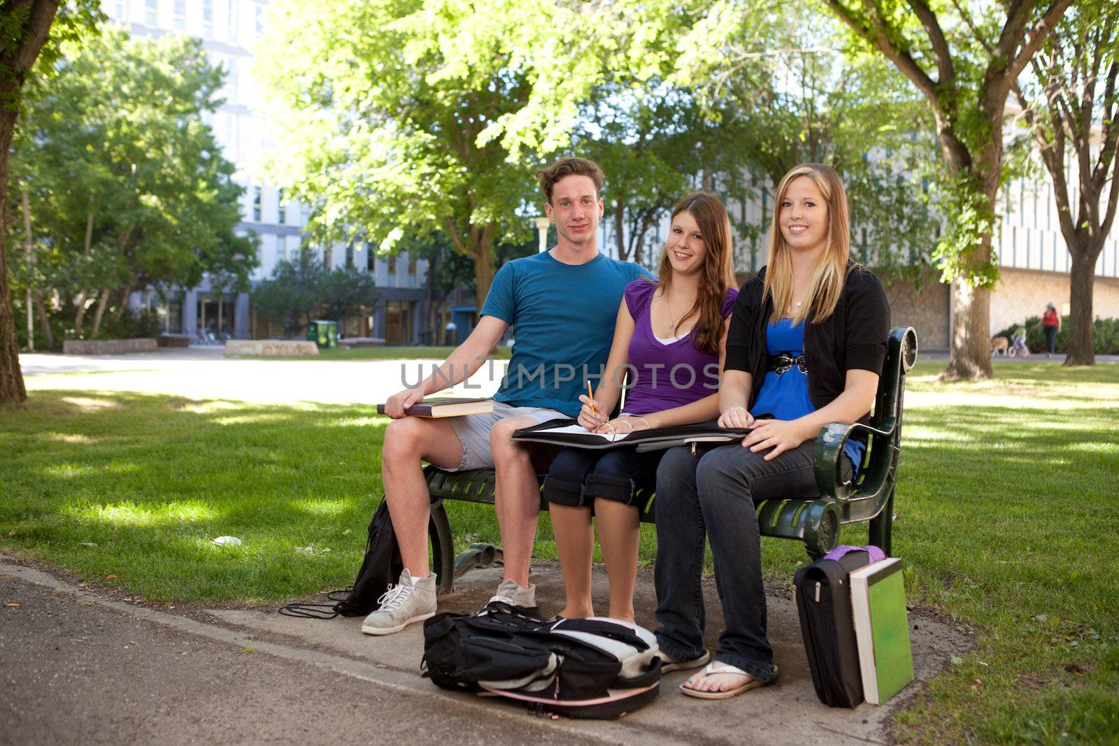 Group of students sitting on a bench on campus looking at the camera