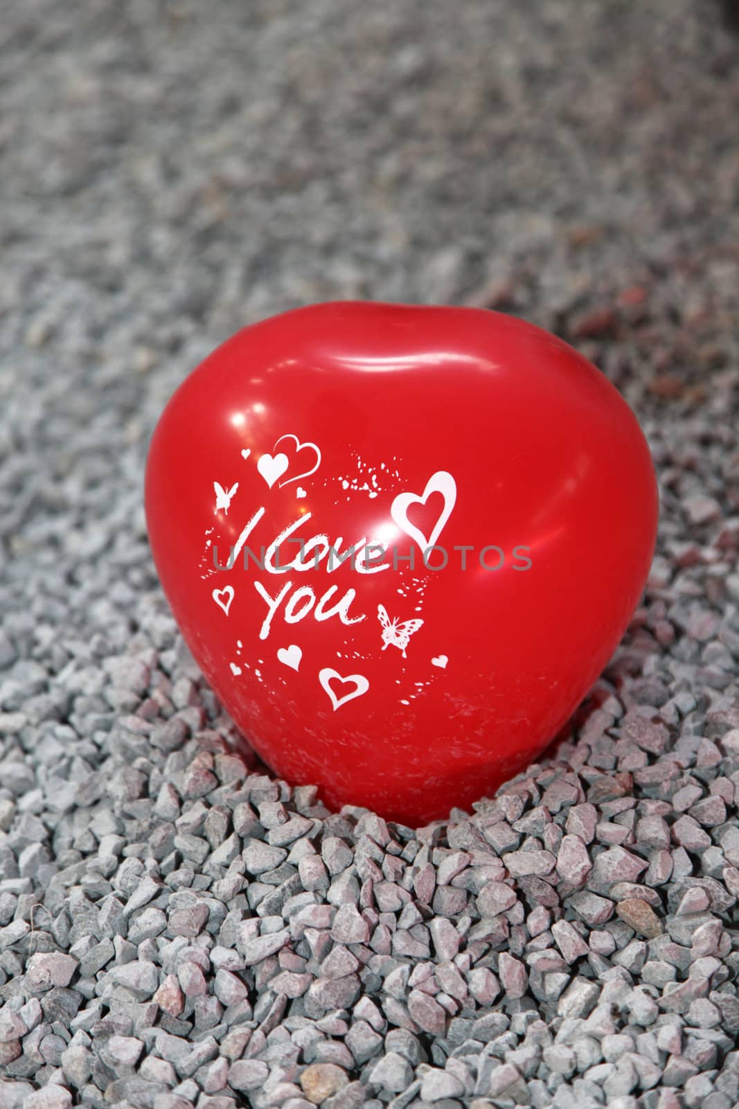 Red shaped heart with "I love uou' inscribed on it sitting on pebbles.