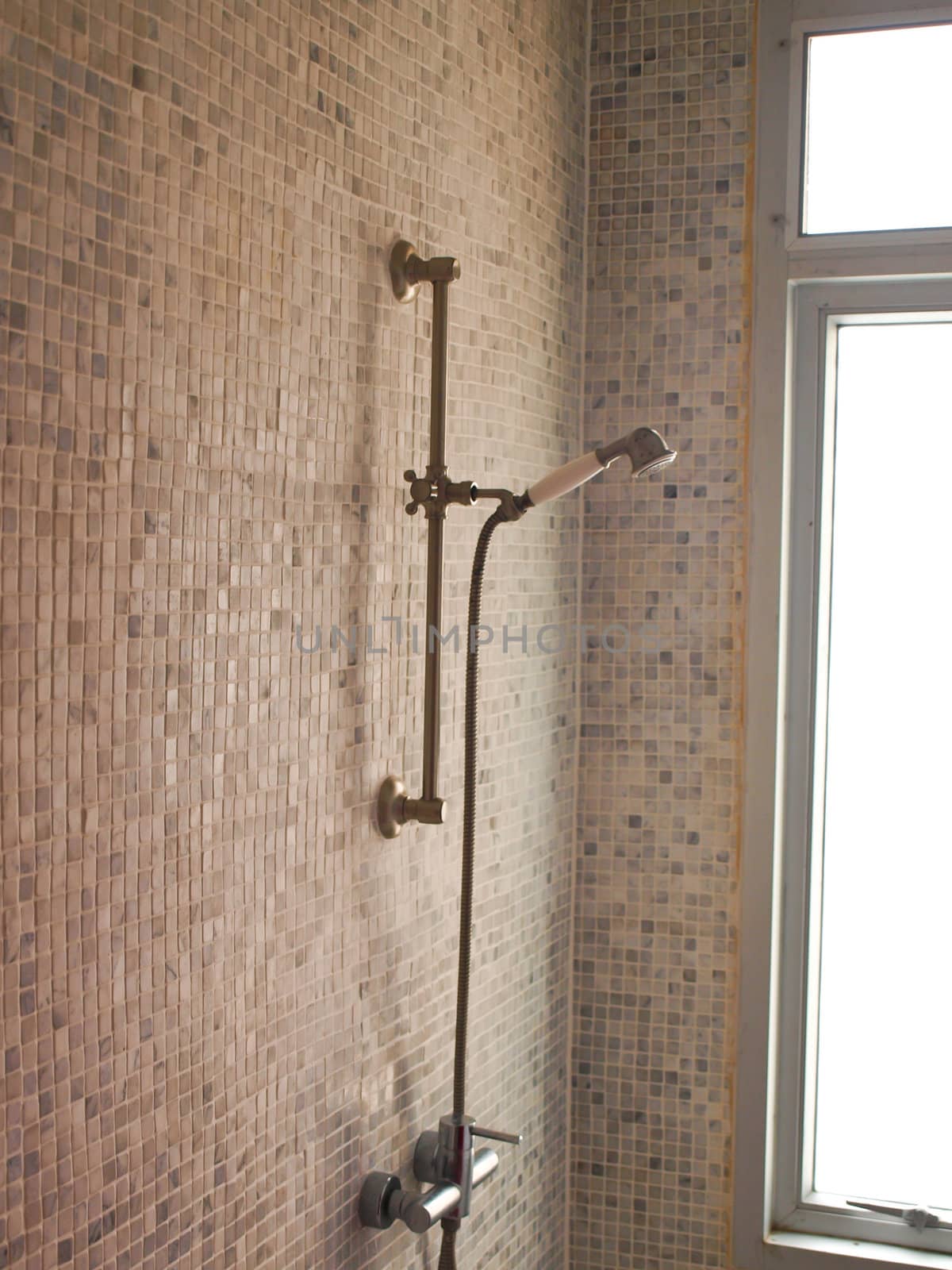Modern shower faucet with light tiled wall and natural light