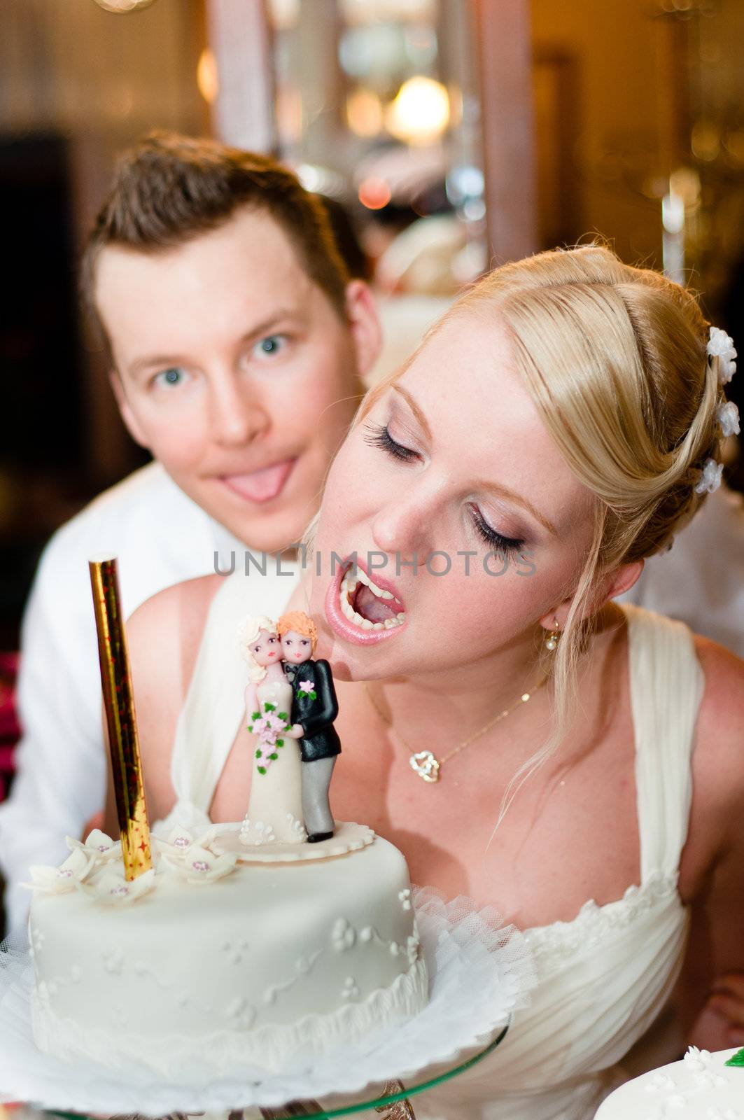Young bride is going to bite her cake with groom in background
