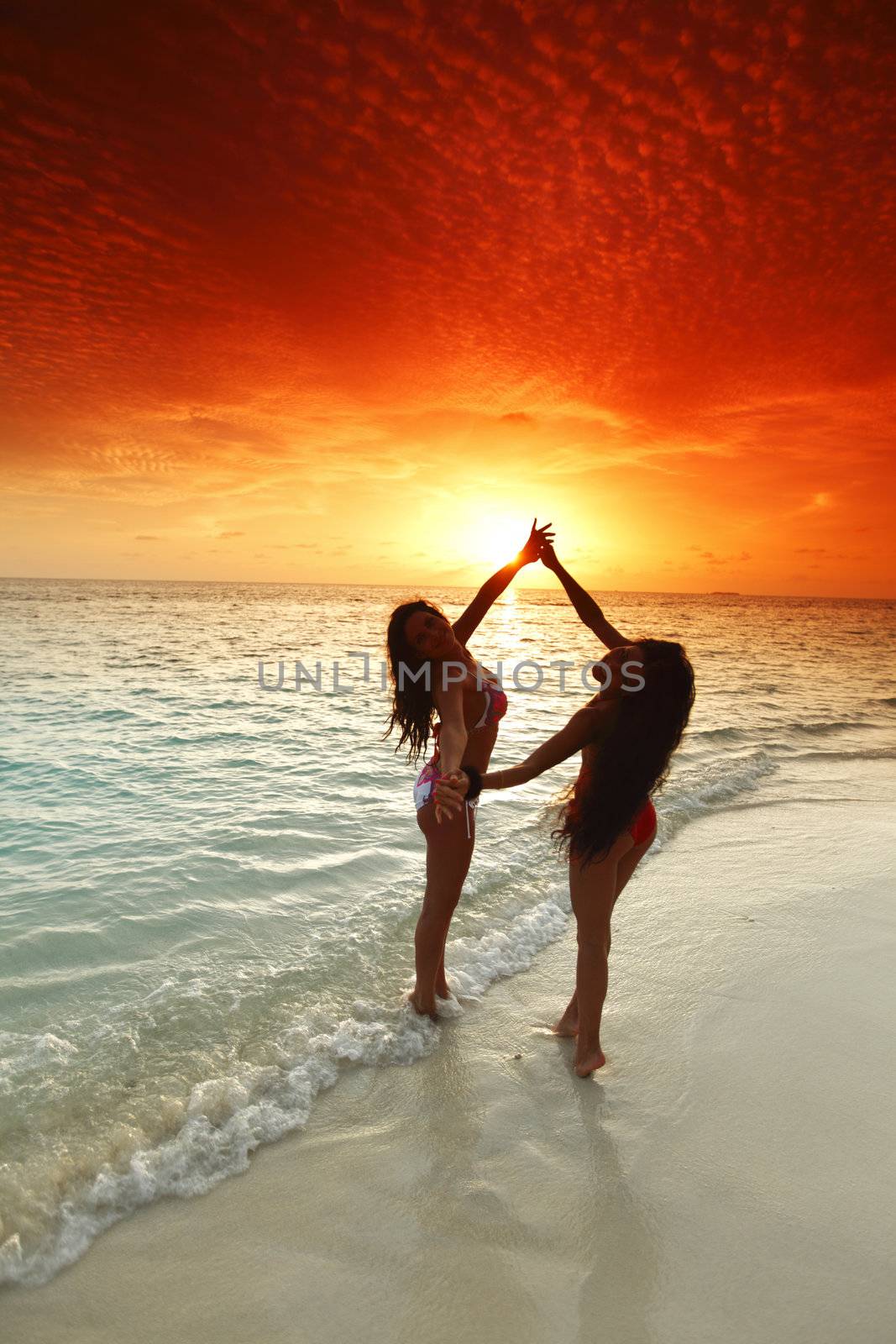 Two beautiful women in bikini enjoying sunset on beach