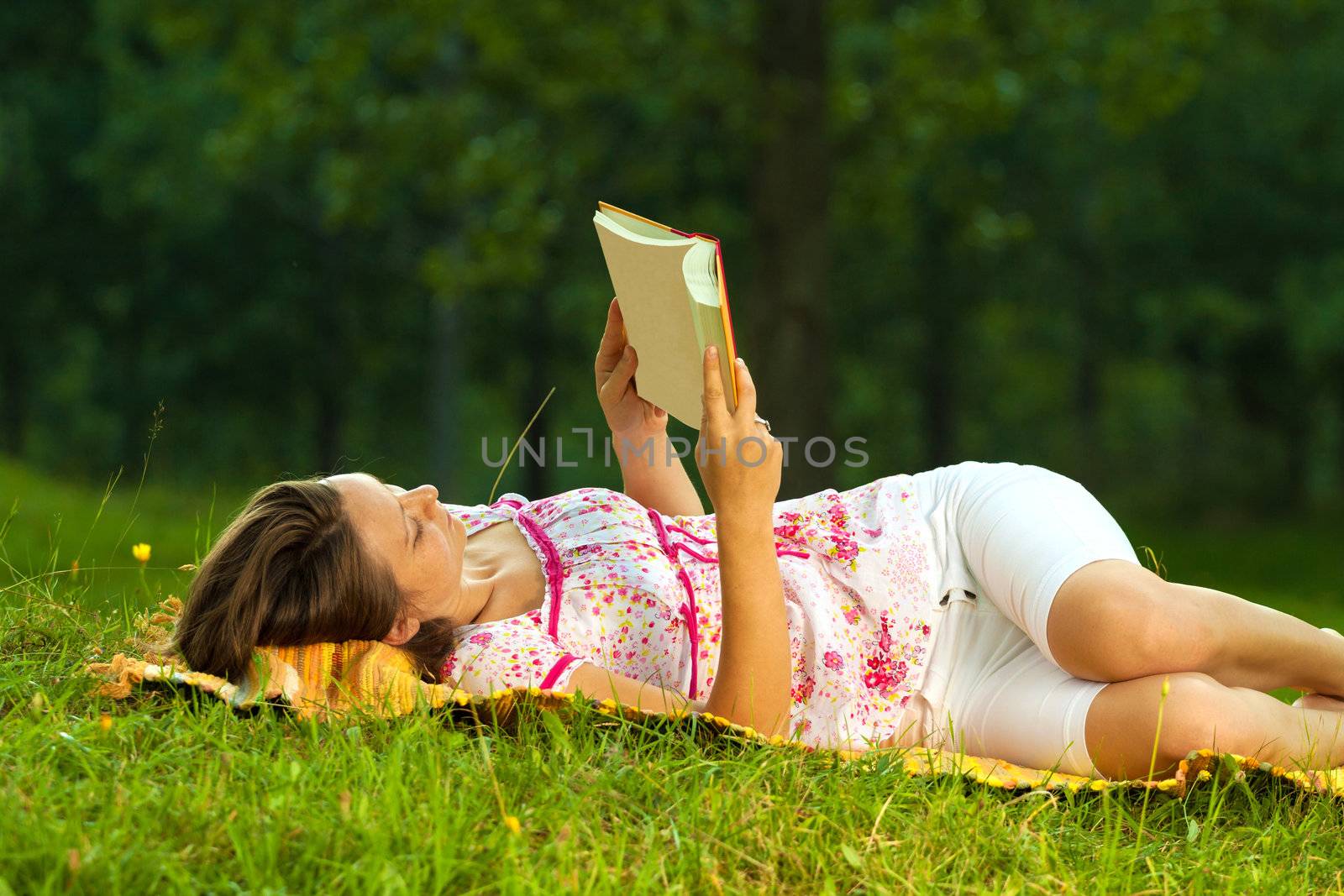 Beautiful young brunette reading on a meadow in the park by Lamarinx
