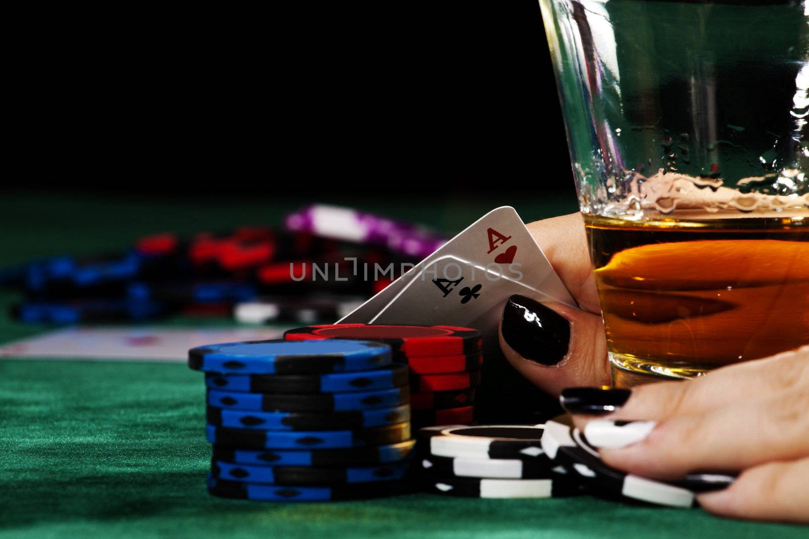 Lady with black manicure holding a great poker hand next to a glass of whisky.