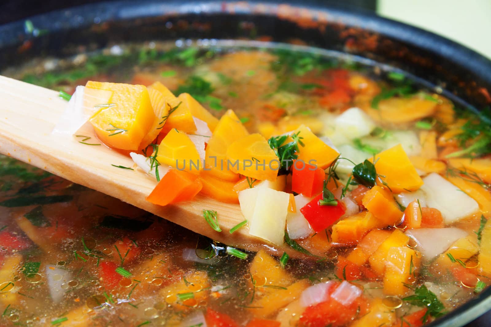 Vegetable soup with carrots, paprika, potatoes, onions and parsley with a wooden spoon