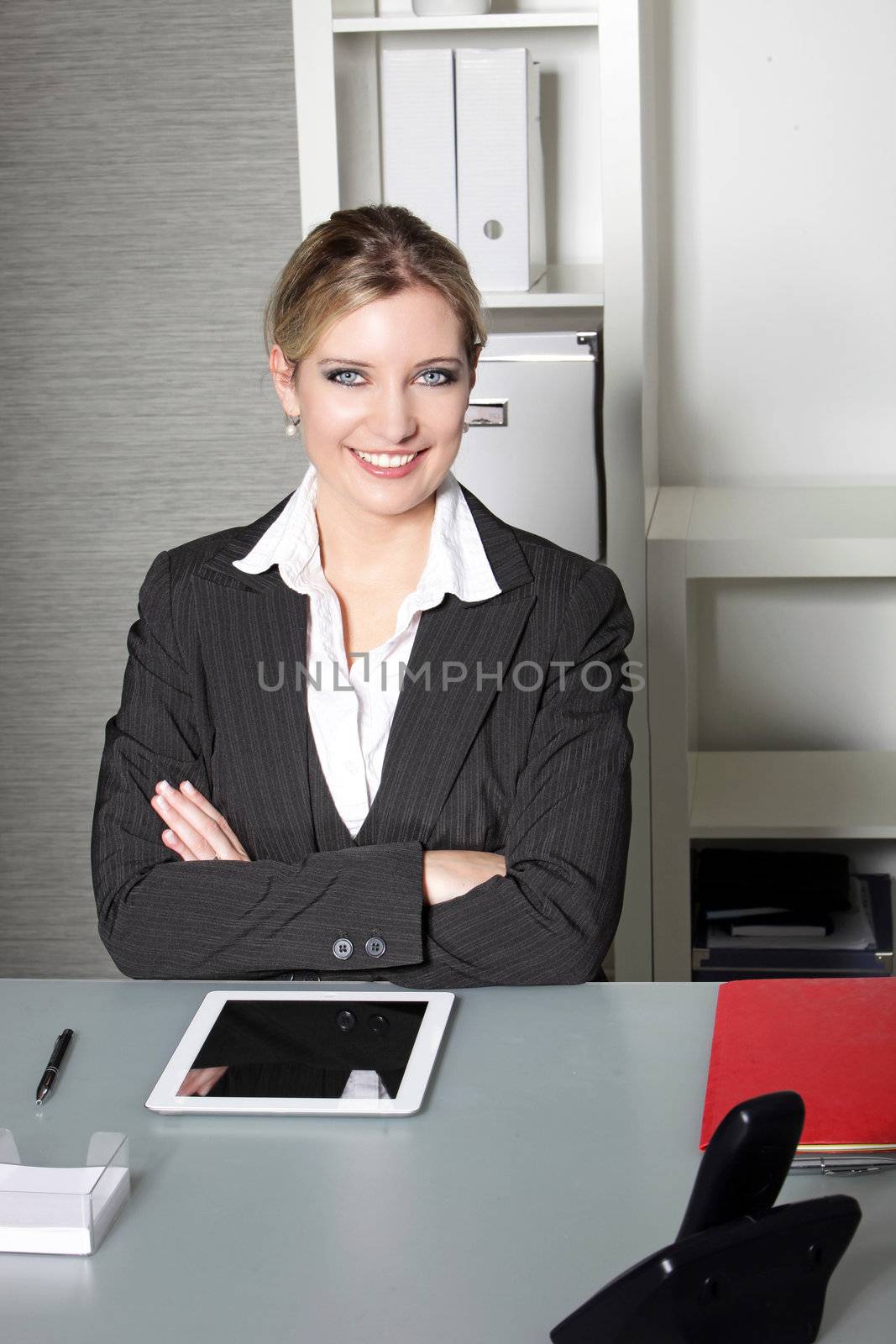 Confident successful businesswoman sitting at her desk with her arms folded smiling at the camera