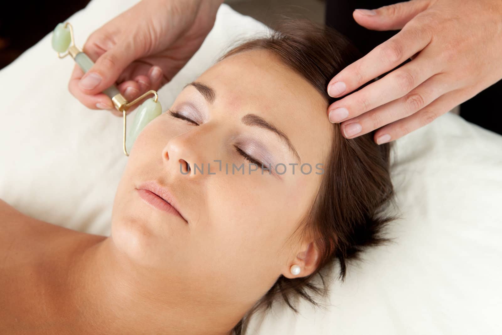 Attractive female reciving face massage with jade roller at acupuncturist
