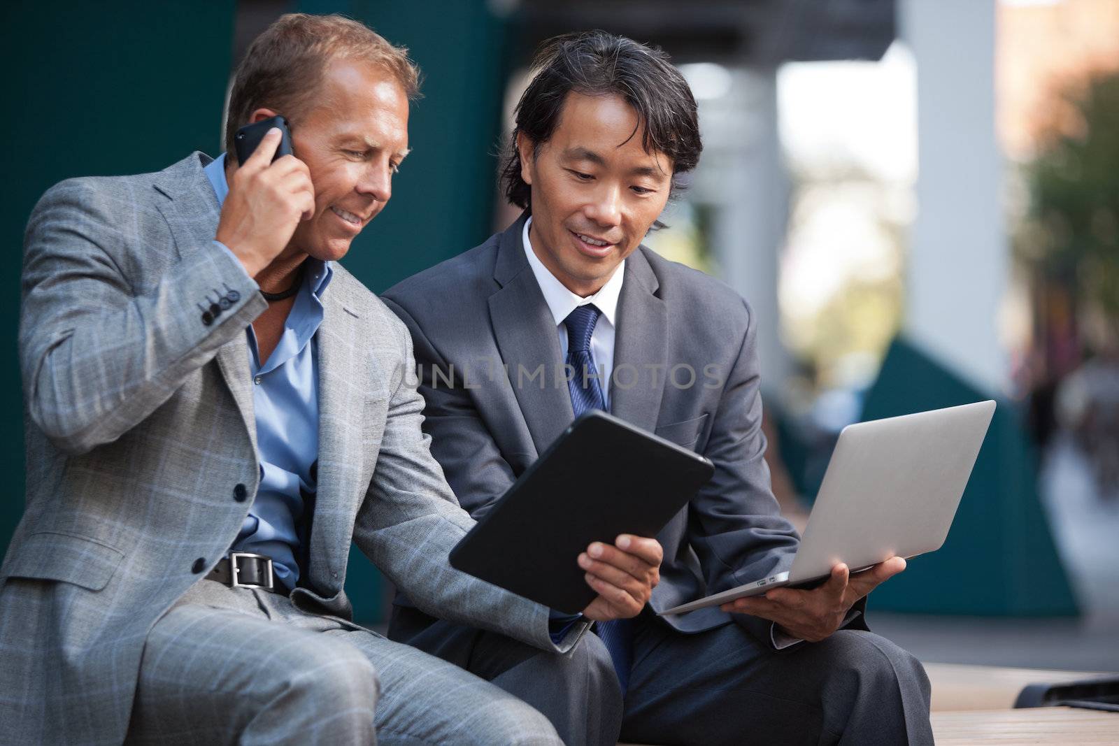 Businessmen using electronic gadgets by leaf