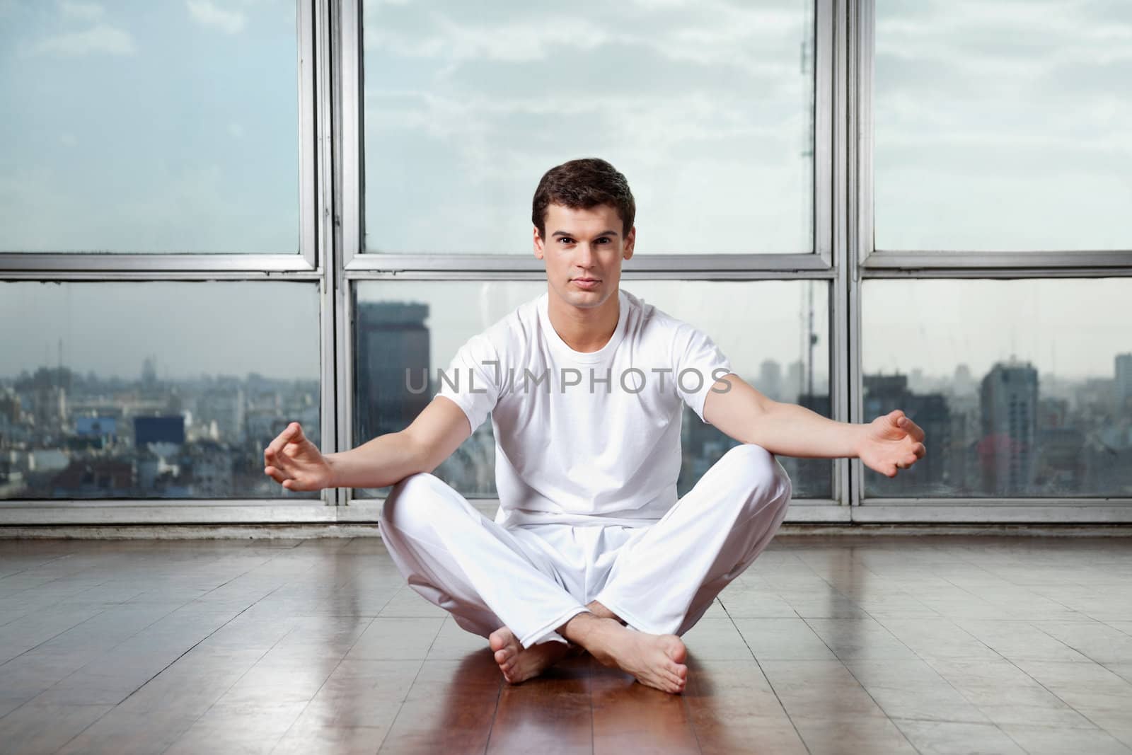 Full length portrait of a young man meditating in lotus position at gym