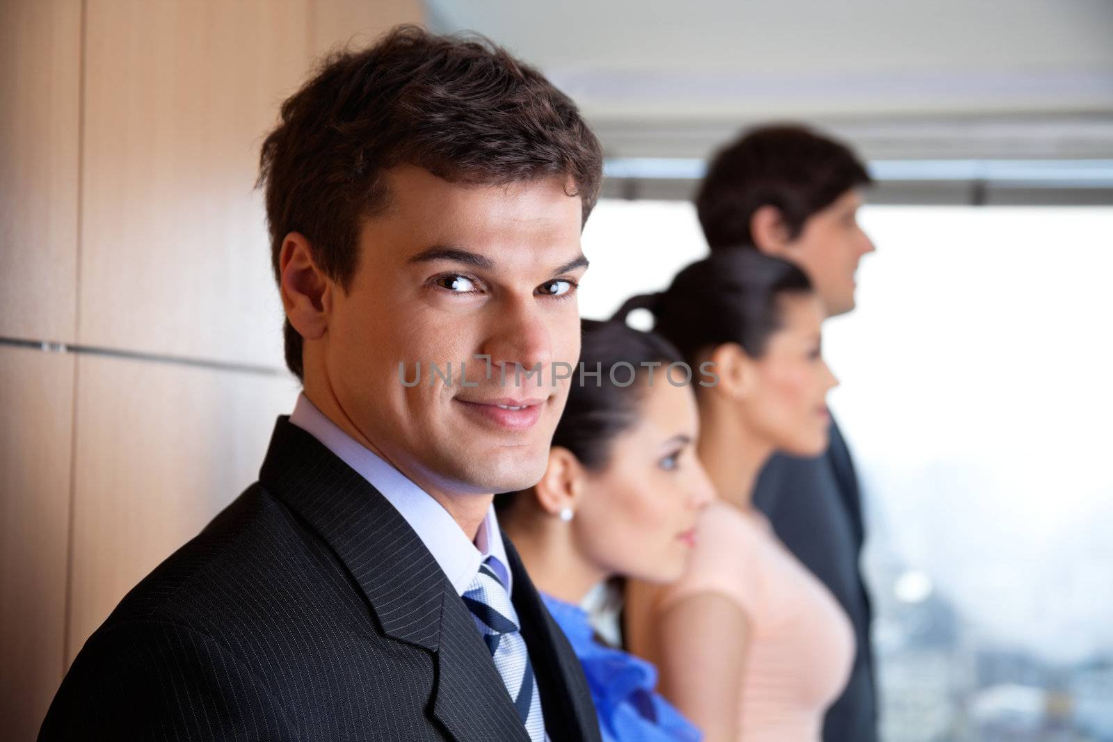 Portrait of handsome male executive smiling with colleagues standing besides him