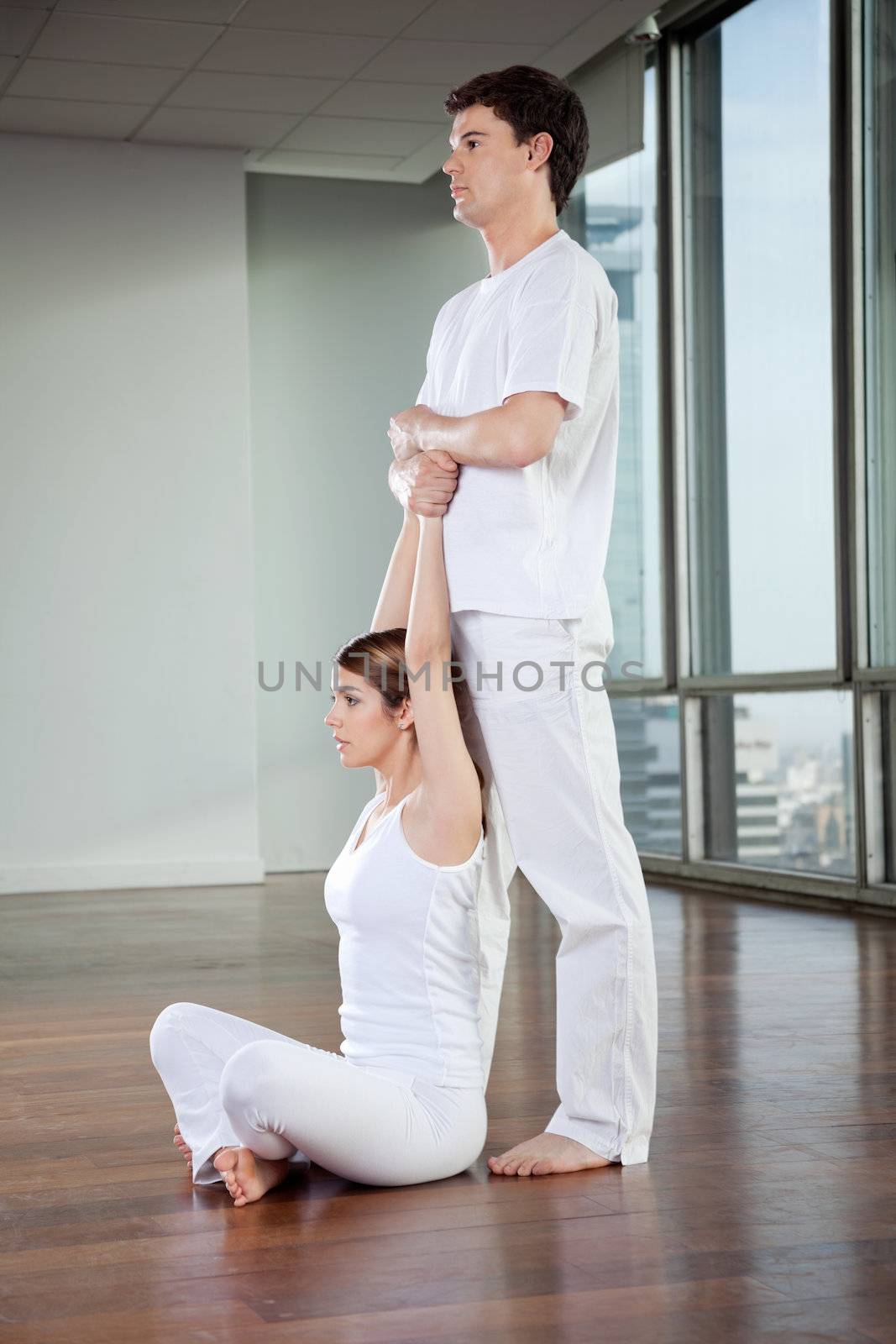 Yoga instructor teaching yoga positions to young woman at gym
