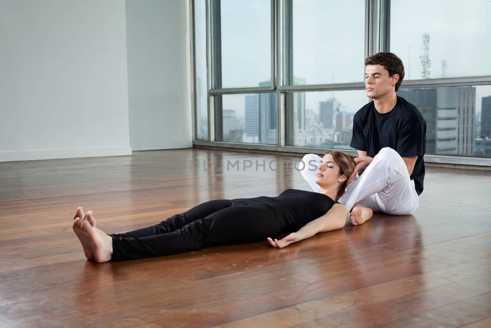 Young male yoga instructor helping female trainee with a pose at gym