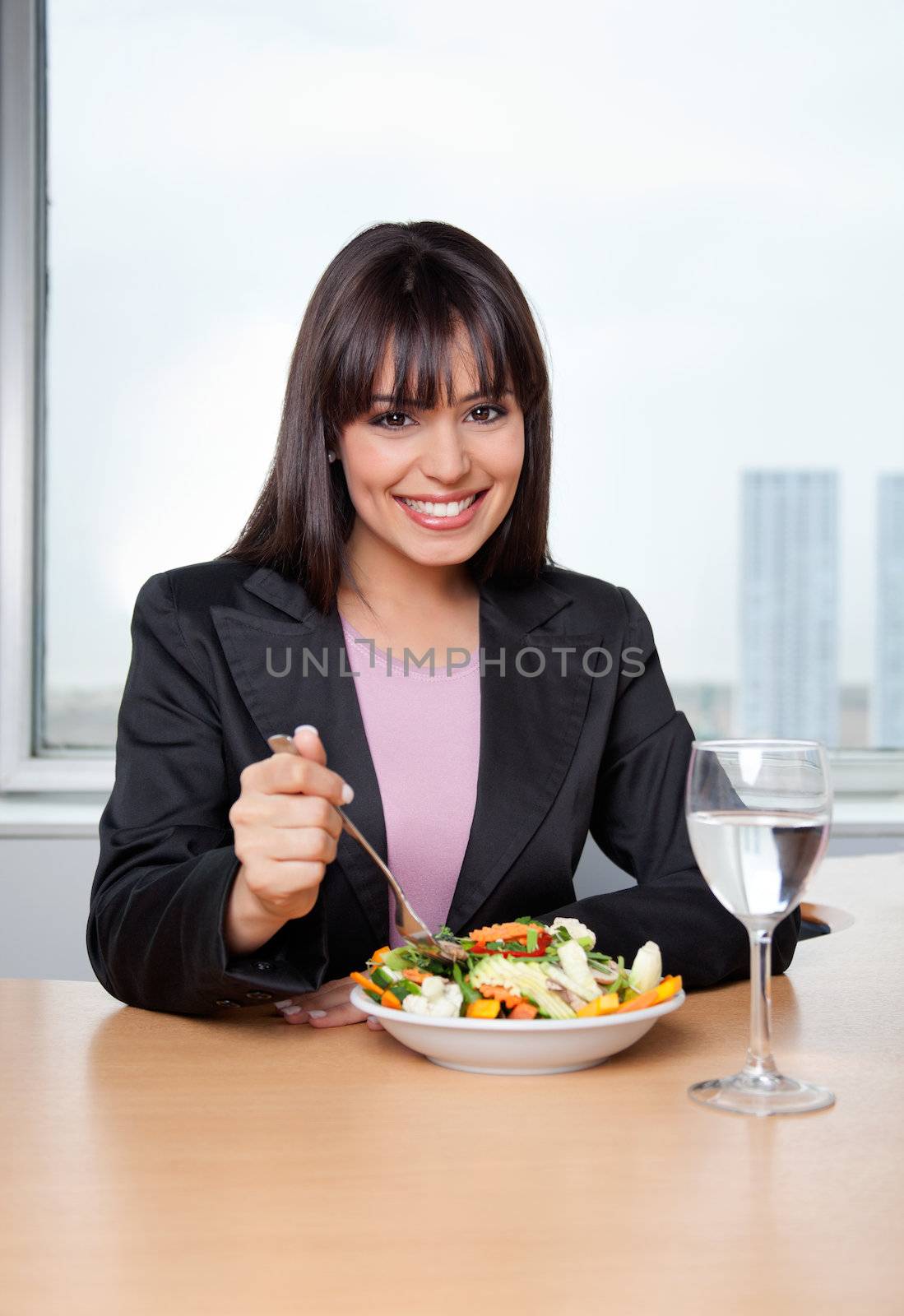 Portrait of smiling businesswoman having fresh vegetable salad with glass of water on desk