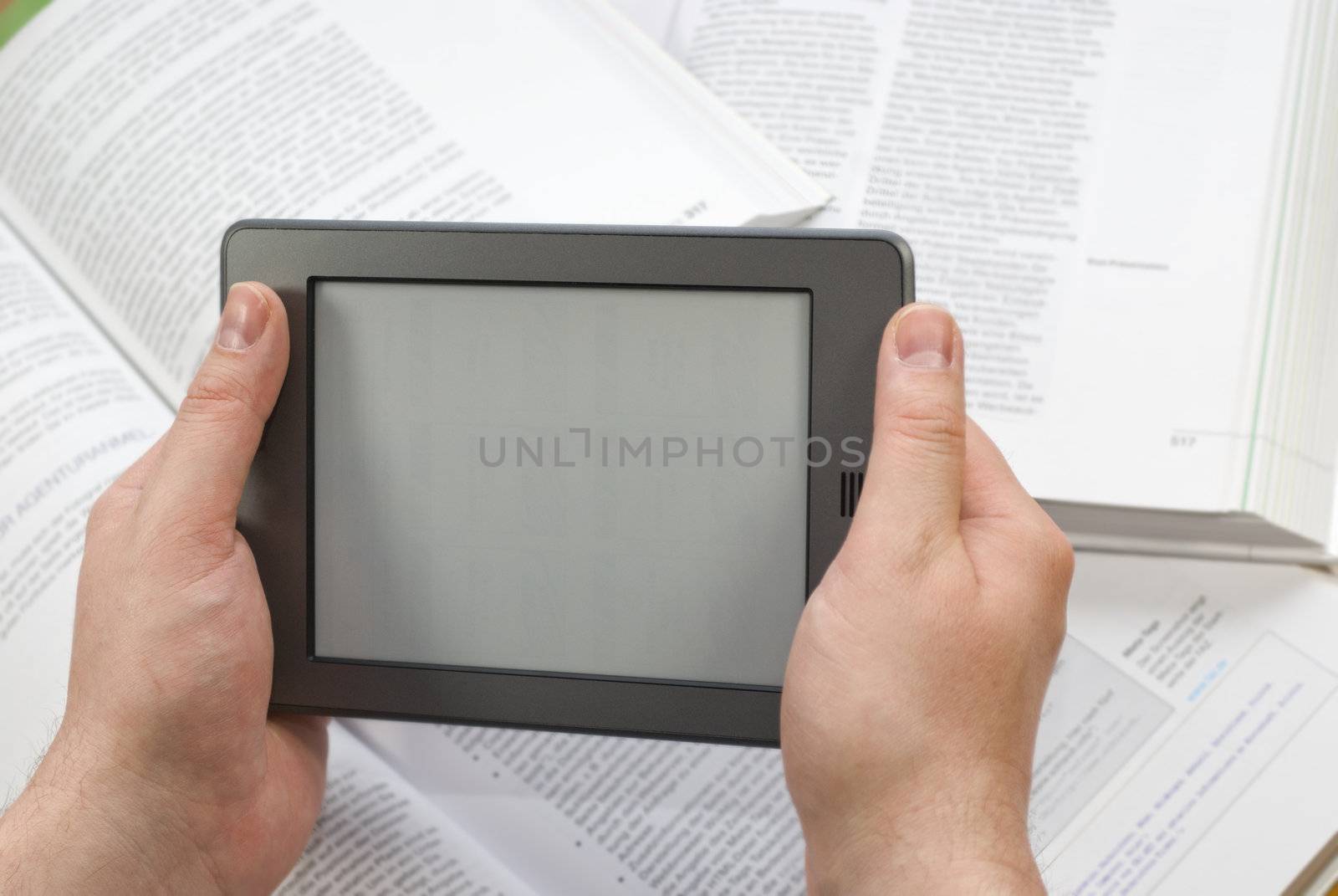 Man hands holding  an electronic book reader with blank screen, open books in the background