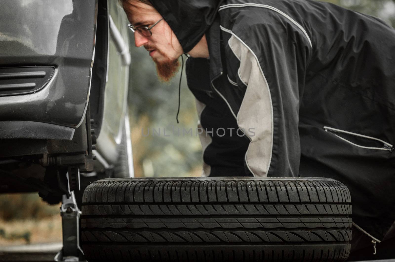 Young adult inspecting the wheel of a car