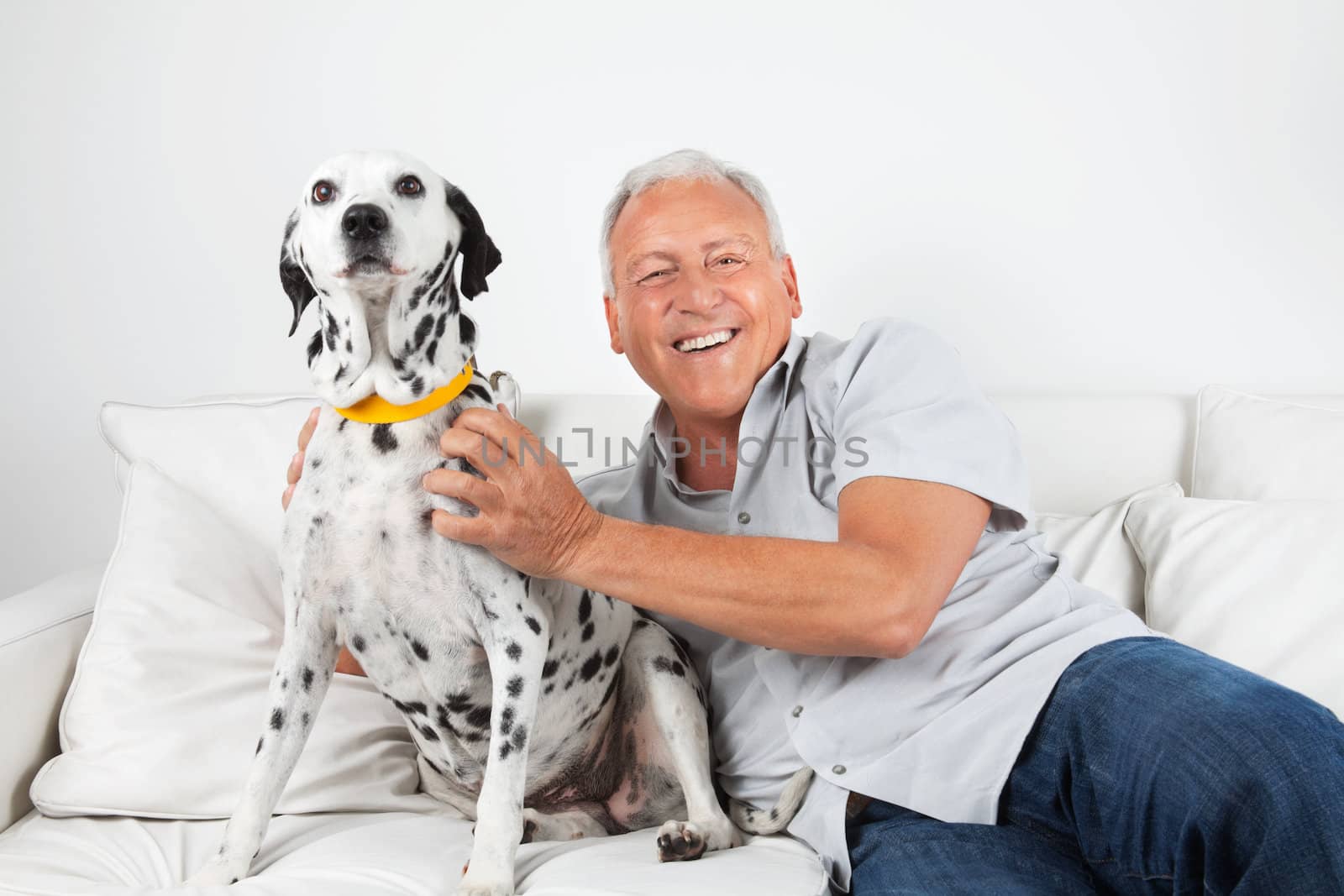 Portrait of happy casual senior man sitting with his pet dog on sofa