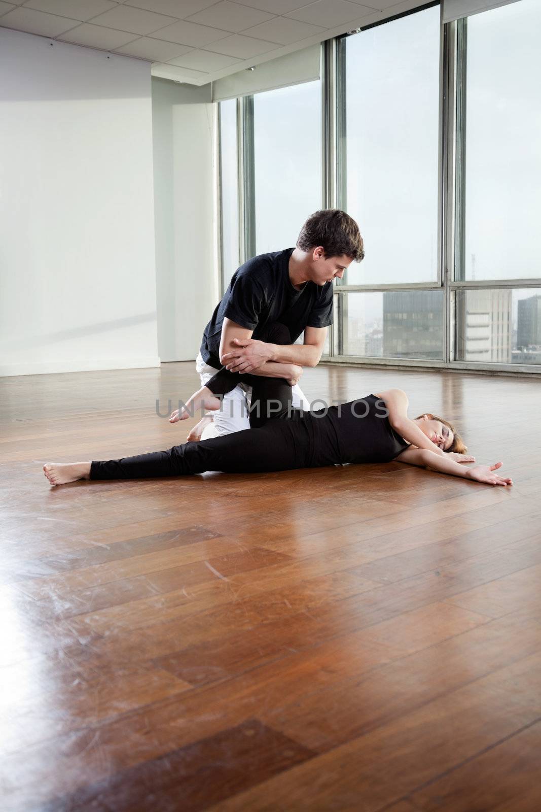 Young male yoga instructor helping female trainee in yoga exercise at gym