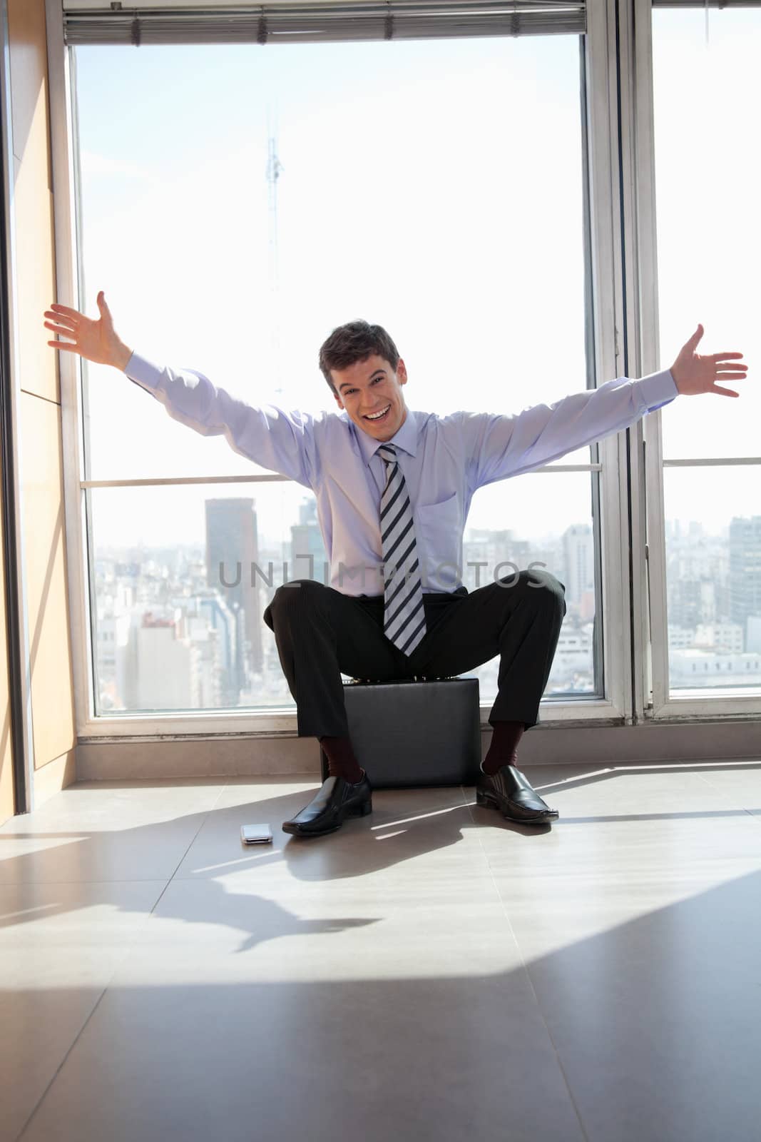 Portrait of excited male entrepreneur sitting on briefcase