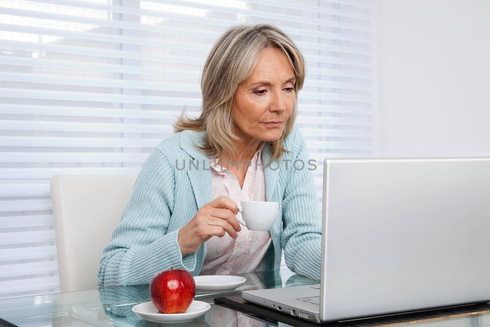 Mature woman working on laptop while holding cup of tea