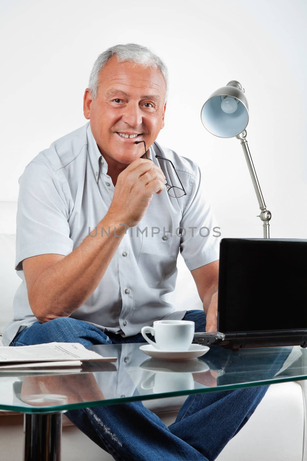 Portrait of smiling senior man sitting with laptop on table at home