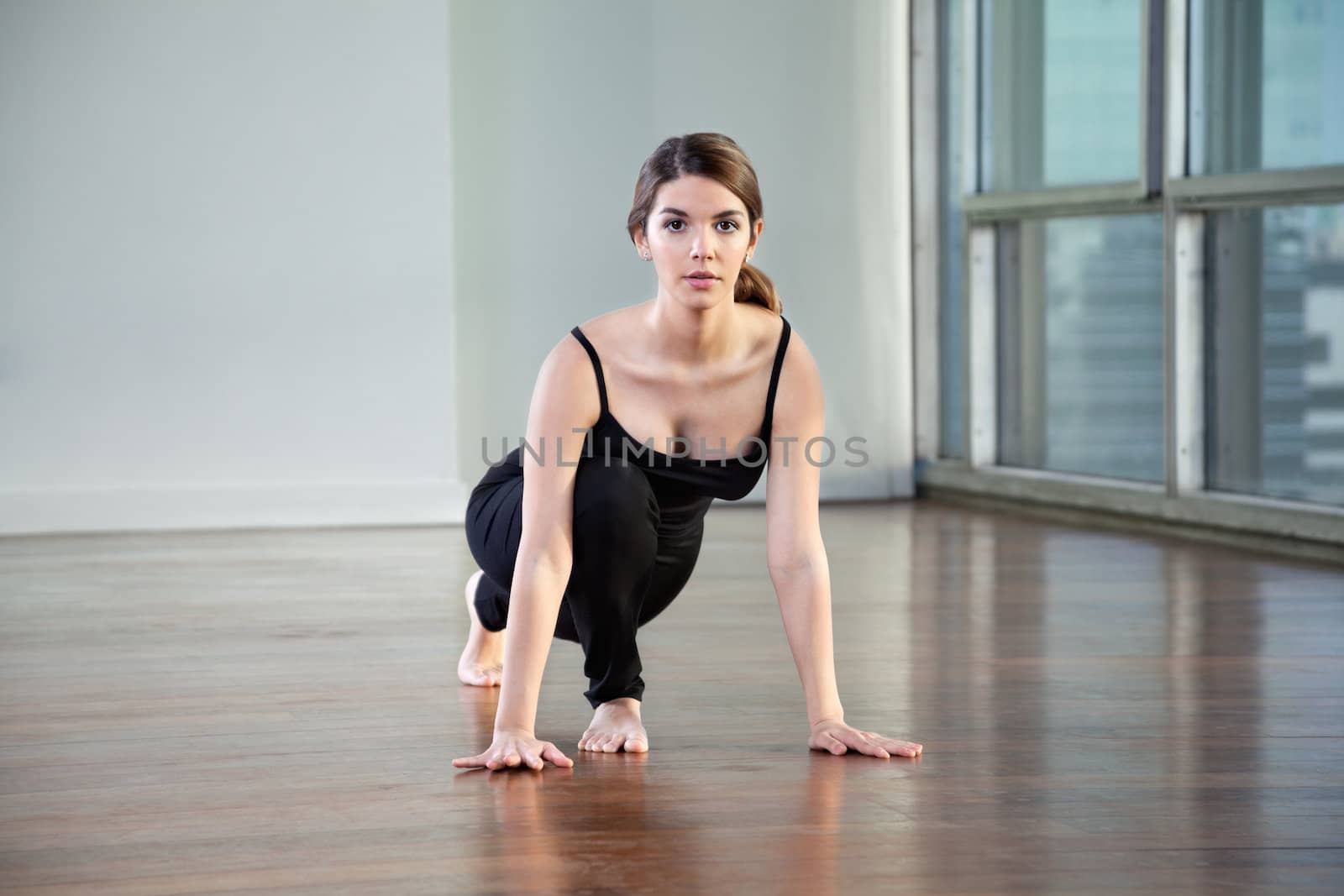 Portrait of a beautiful young woman practicing yoga called Lunge Pose on wooden floor